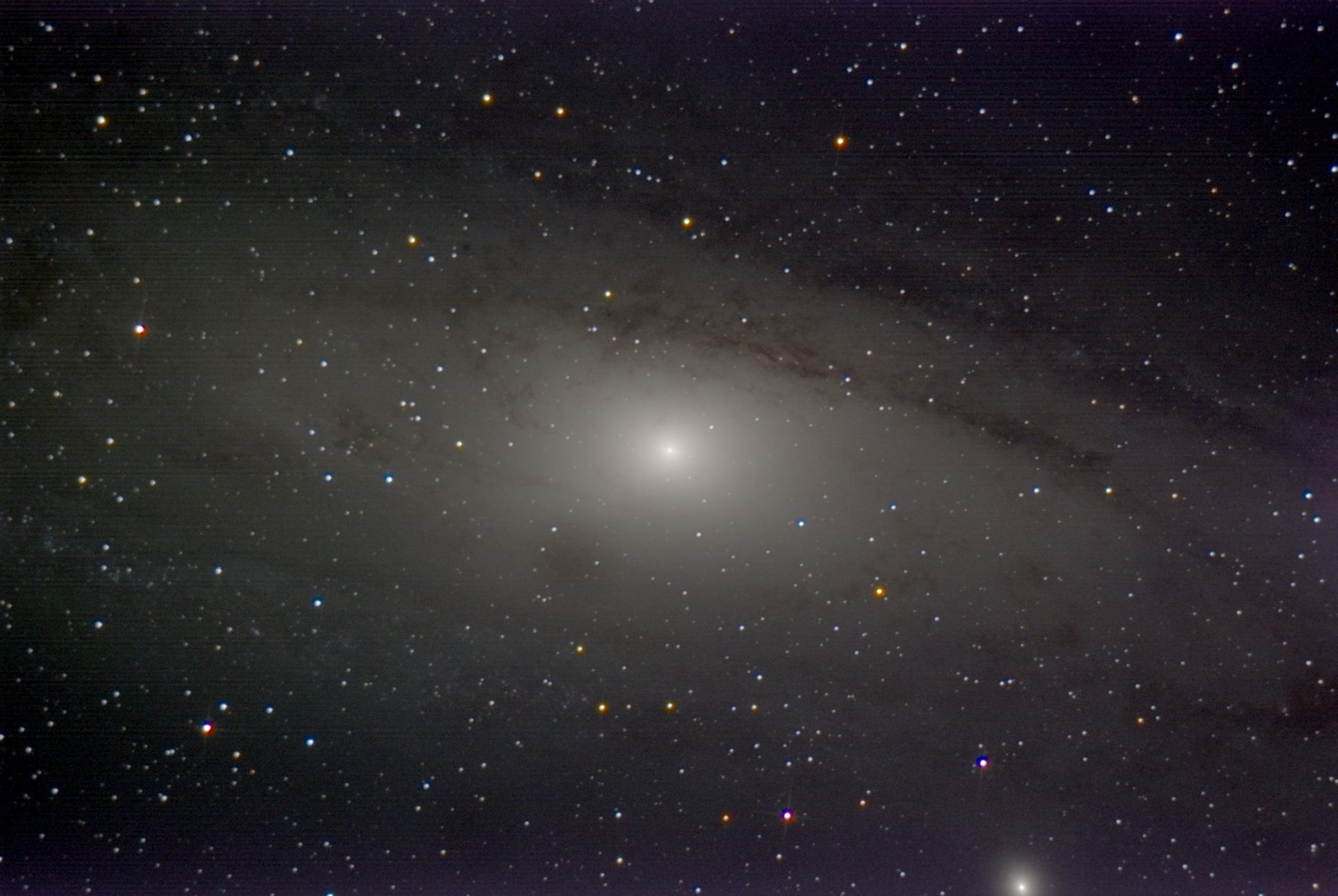 The Andromeda Galaxy across the frame, a bright core with dark dust lanes along its upper edge, and faint horizontal lines across the picture