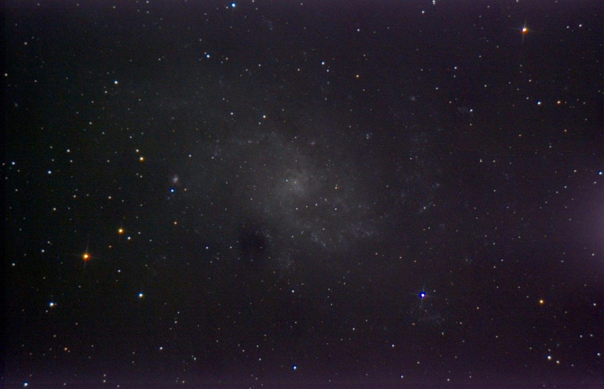 The faint spiral of the Triangulum Galaxy in a field of stars, with a small bright knot to the left of its core